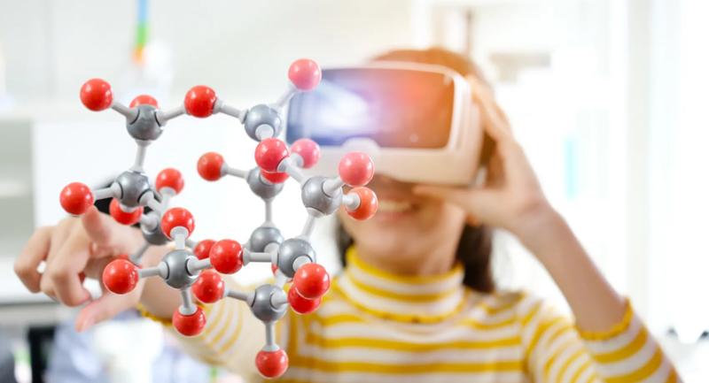 Photo of a girl wearing VR goggles, reaching out to touch a floating molecule strand